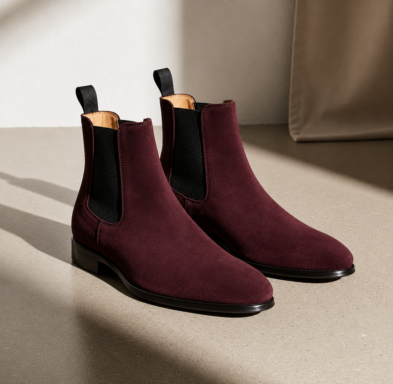 Pair of maroon Chelsea boots on a beige surface with a neutral background