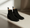 Pair of black Chelsea boots on a light surface with a neutral background