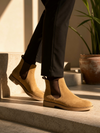 Person wearing tan suede Chelsea boots on a stone step with a plant in the background