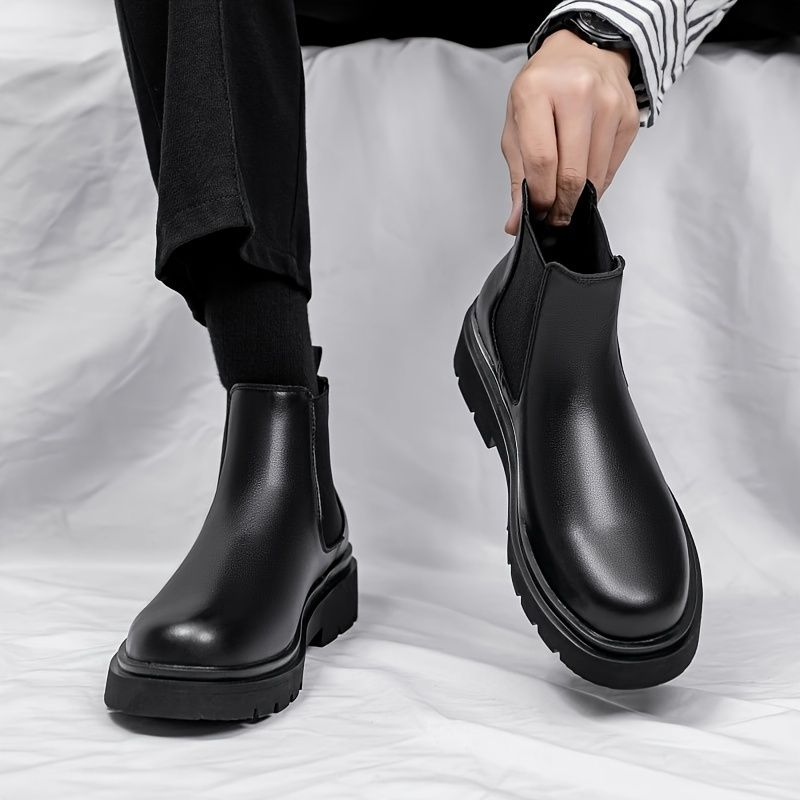 Person wearing black leather Chelsea boots on a white background