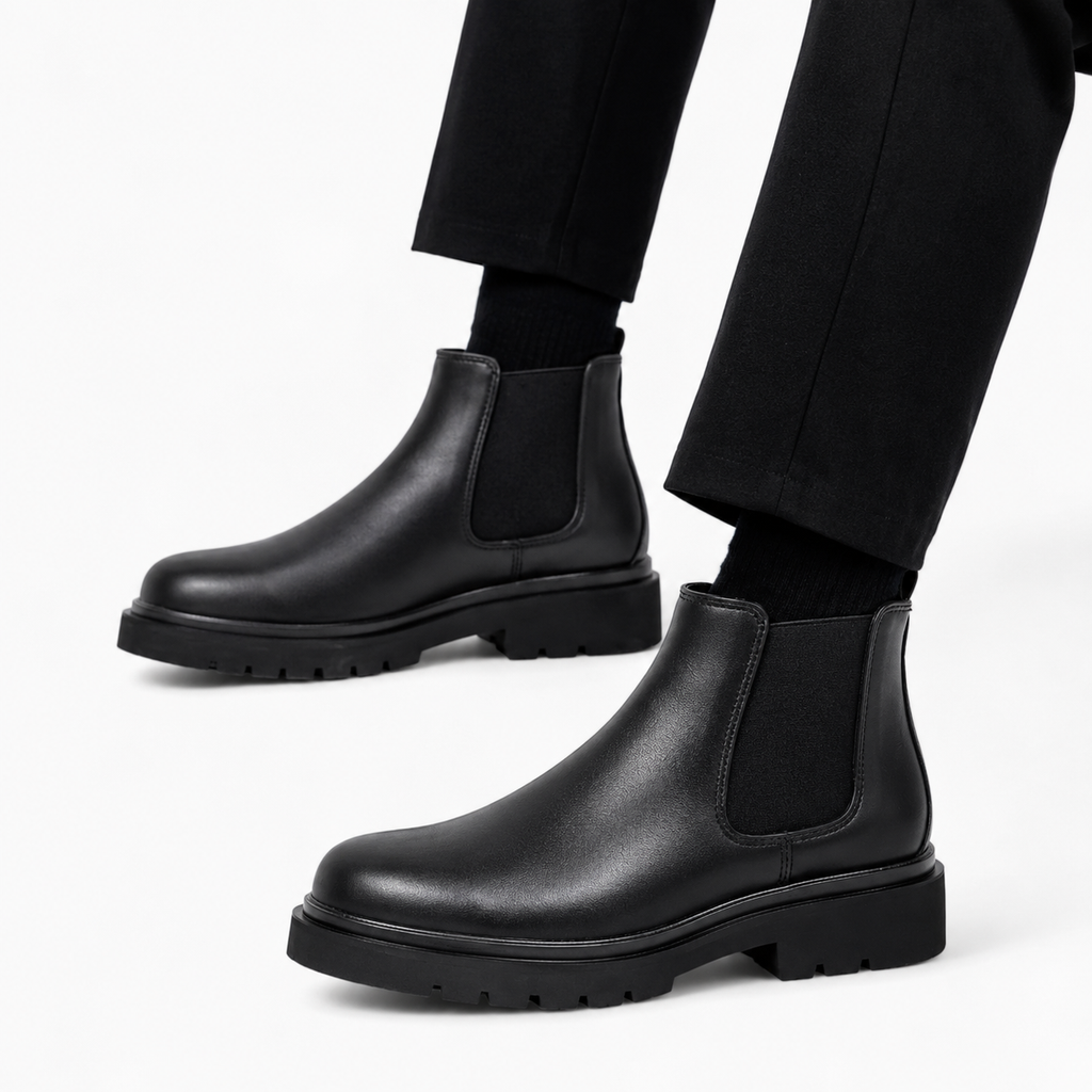 Black leather Chelsea boots worn with black pants on a white background